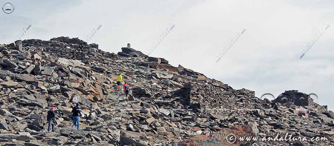 Montañeros subiendo los últimos metros, junto a las ruinas proximas a la cima, hacia el Vértice Geodésico Mulhacén