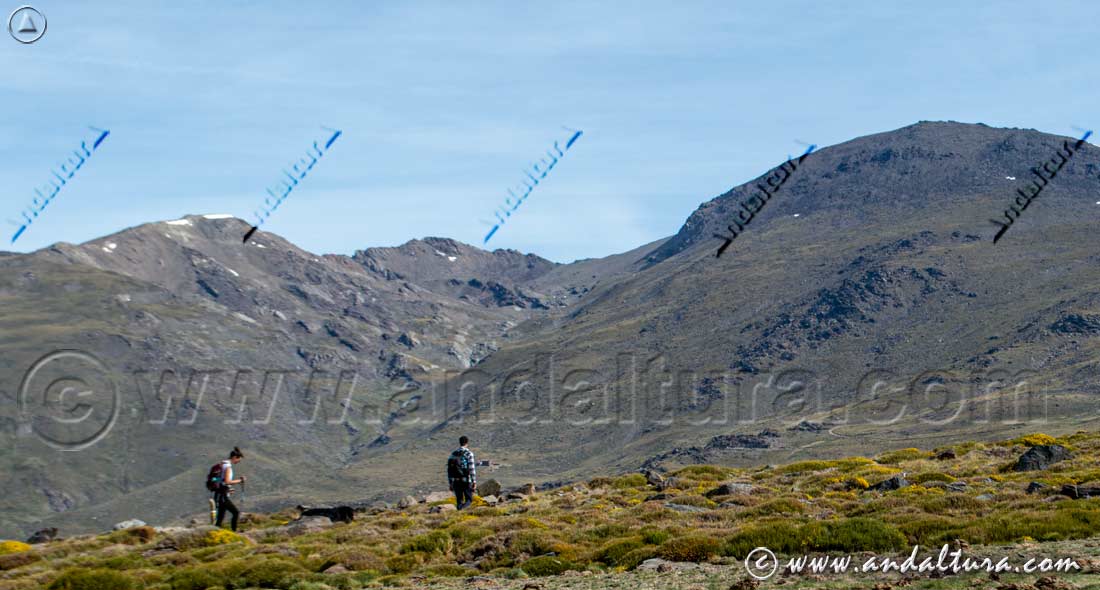 Senderista ascendiendo hacia el Valle del río Mulhacén, al fondo los Tresmiles de Sierra Nevada: Mulhacén, Puntal de la Caldera y Puntal de Loma Pelá