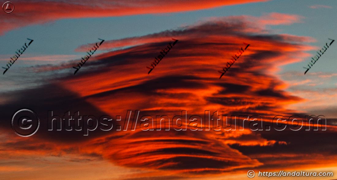 Detalle ampliado de una nube lenticular con intensos colores rojos y anaranjados al amanecer en el cielo de Andalucía